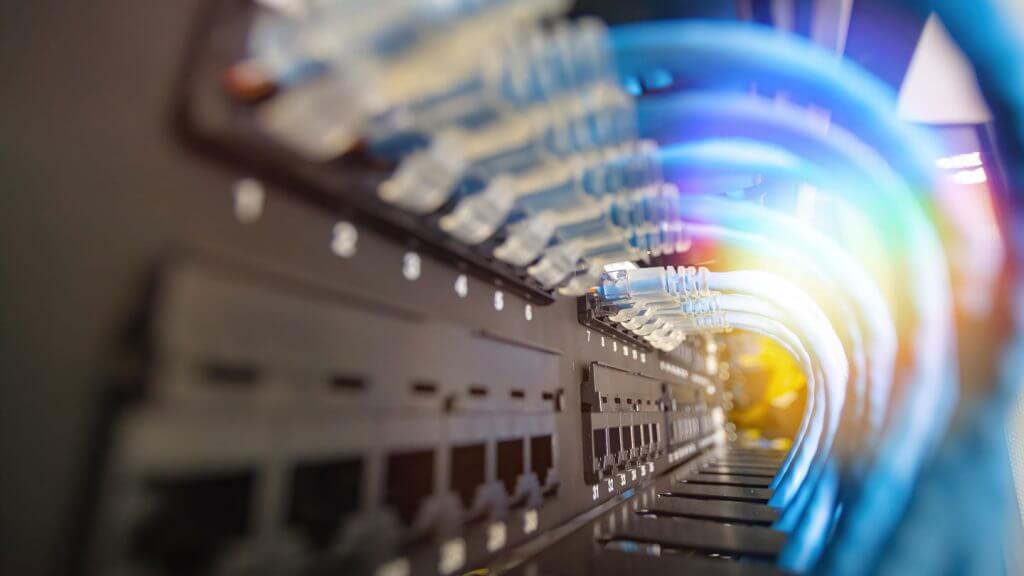 Close-up of several blue Ethernet cables plugged into a network switch, with numbers labeling the ports and a soft, colorful light effect in the background—showcasing reliable Cabling Solutions Dallas.