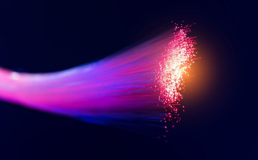 Close-up of a glowing fiber optic cable with strands emitting vibrant pink and purple light against a dark background, showcasing advanced Cabling Solutions Dallas.